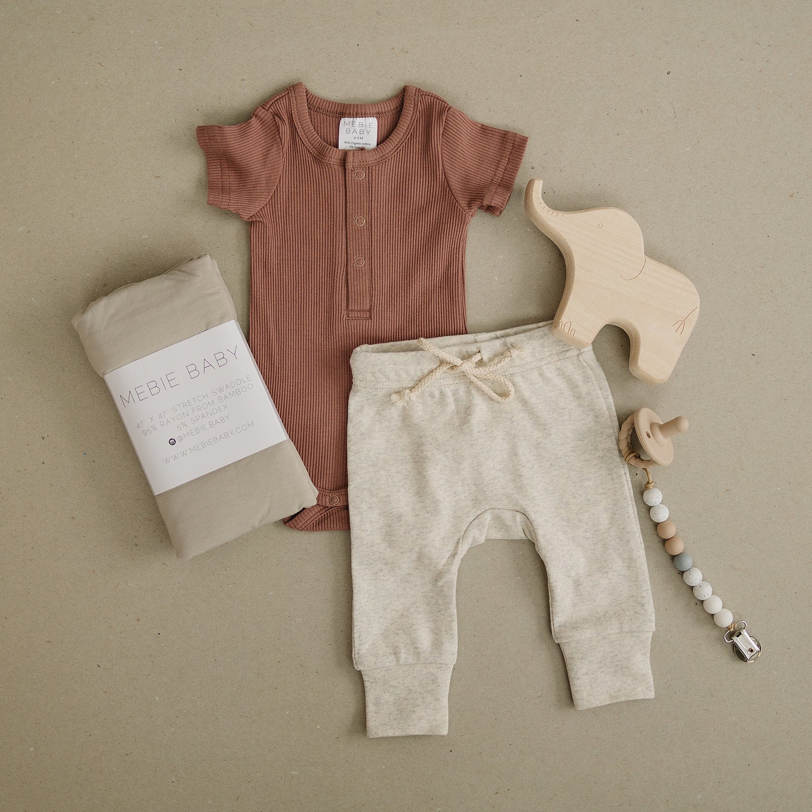 Baby outfit with brown romper, beige pants, and wooden toys on a beige background