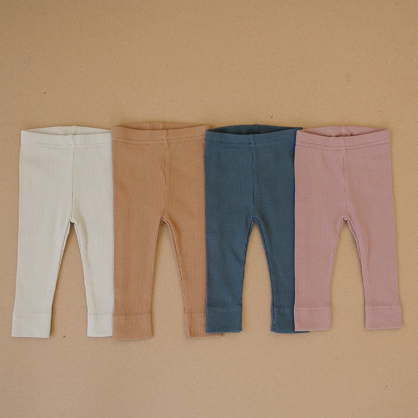 Four pairs of ribbed leggings in different colors on a beige background