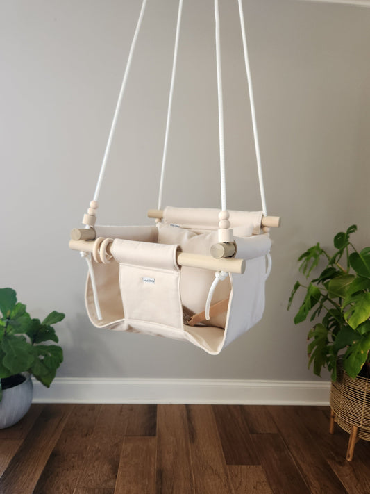 Children's swing hanging against a plain wall with plants on either side.
