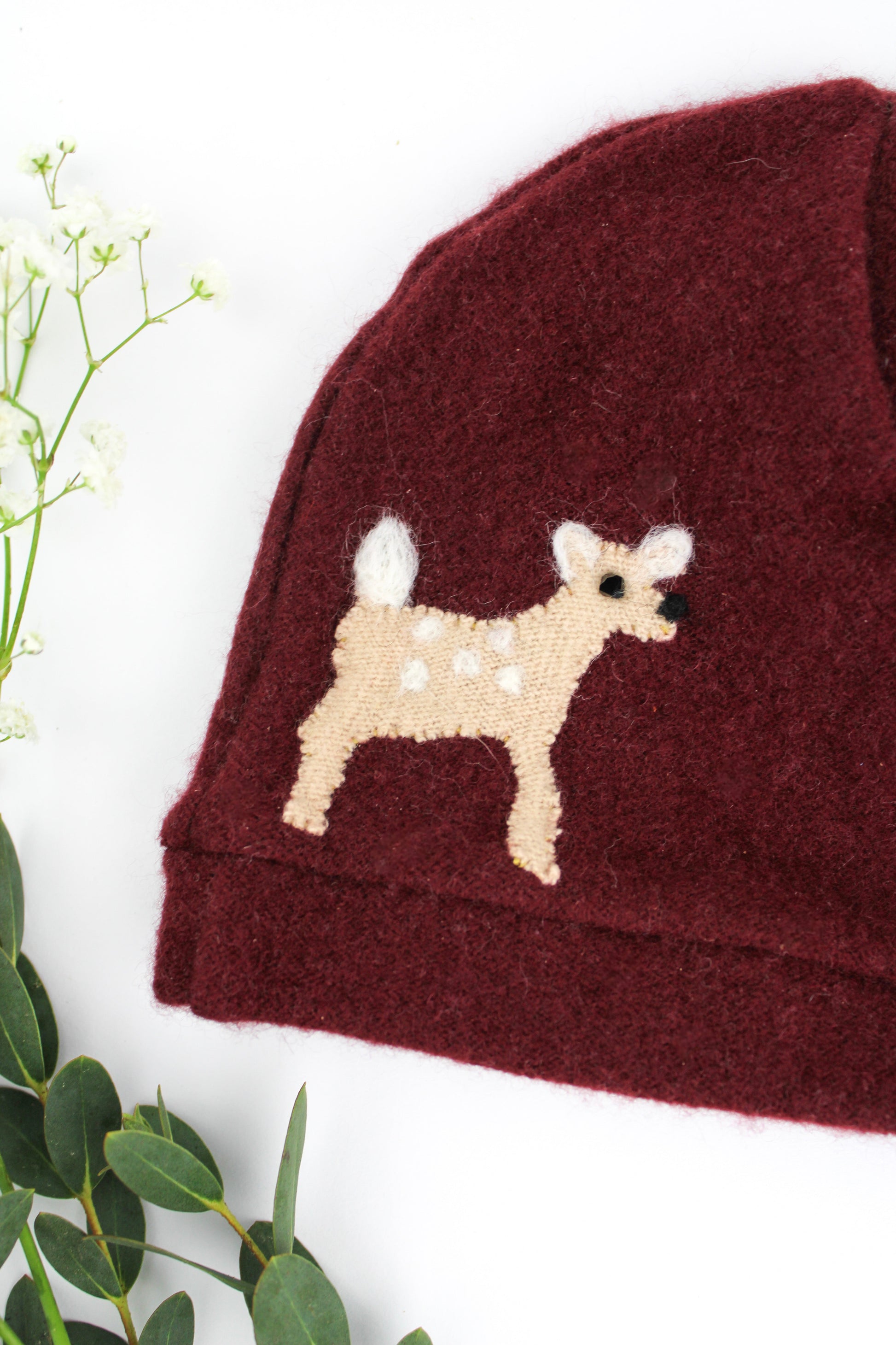 Maroon baby hat with a white deer design on a white background
