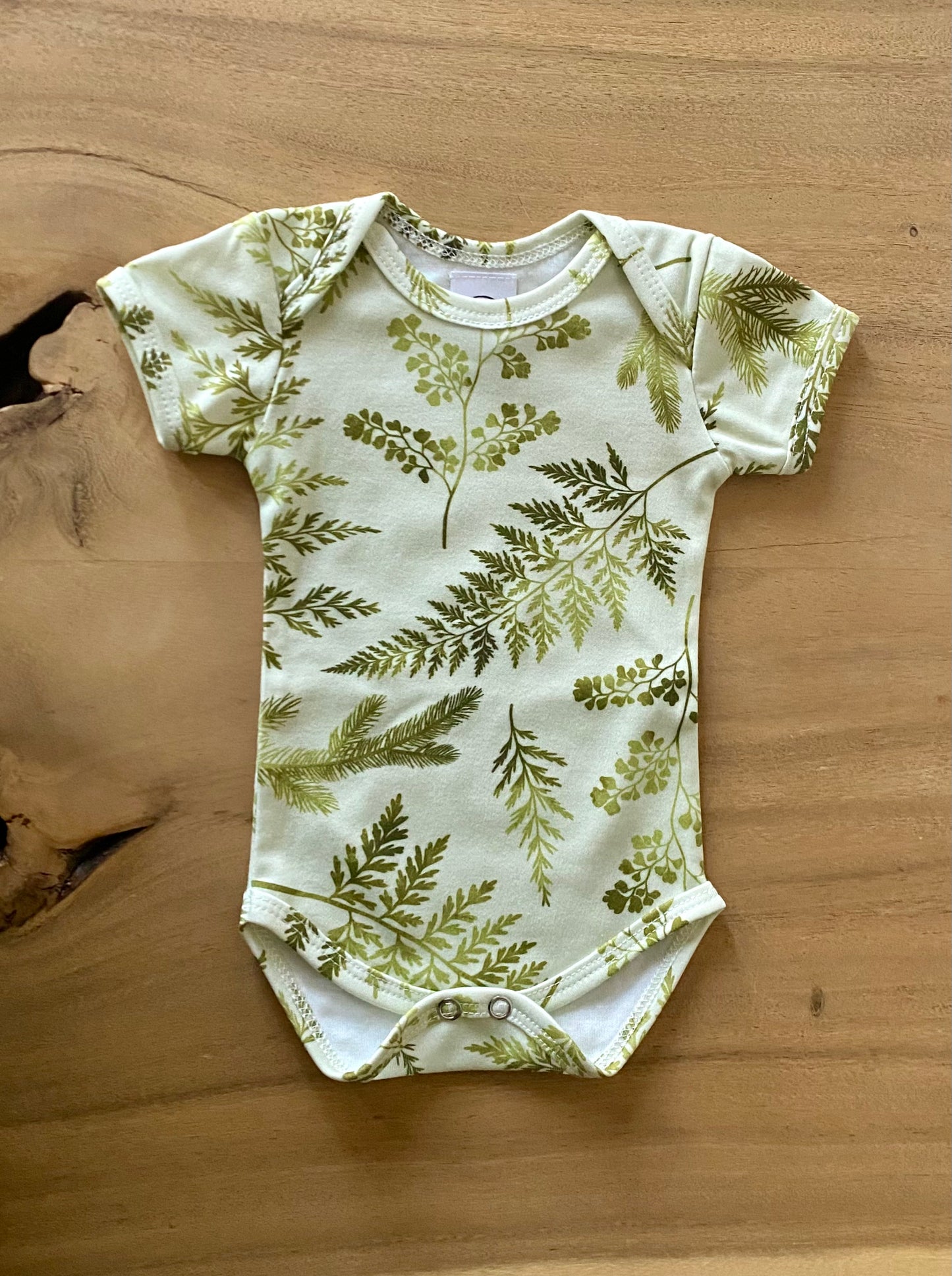 Baby onesie with green leaf pattern on a wooden surface
