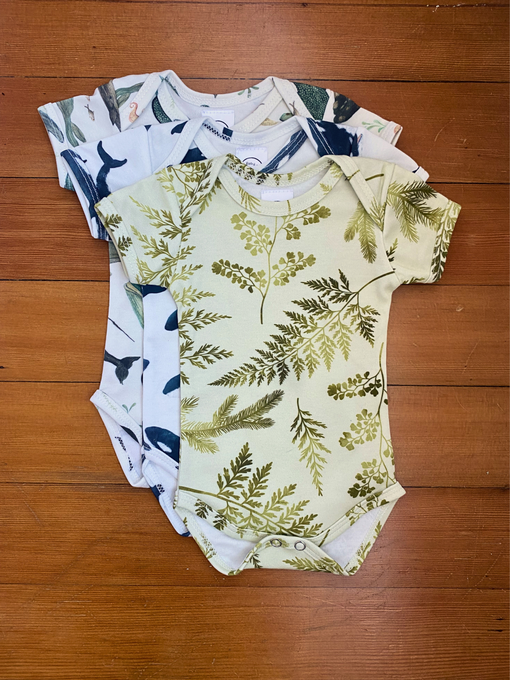 Three baby rompers with different patterns on a wooden surface