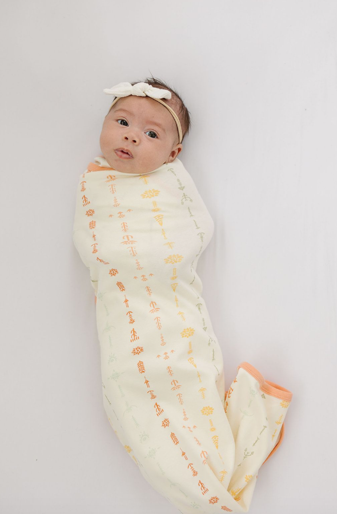 Newborn baby wrapped in a patterned swaddle on a plain background