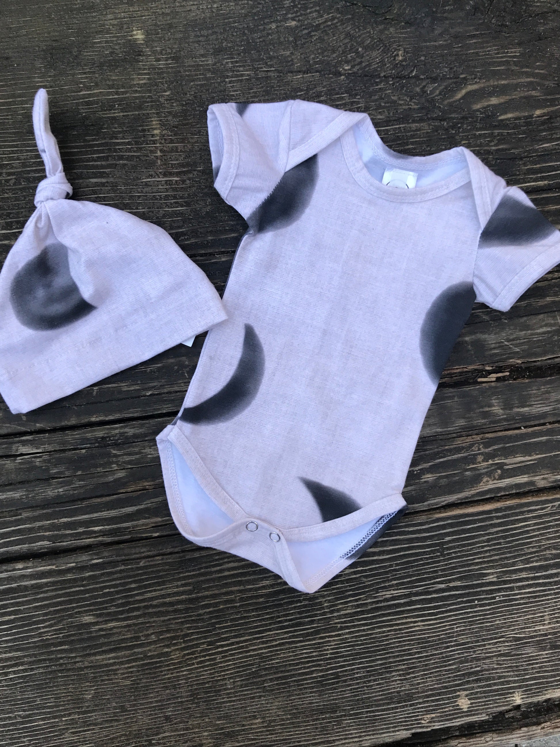 Short sleeve moon phase onesie with hat  on a wood bench