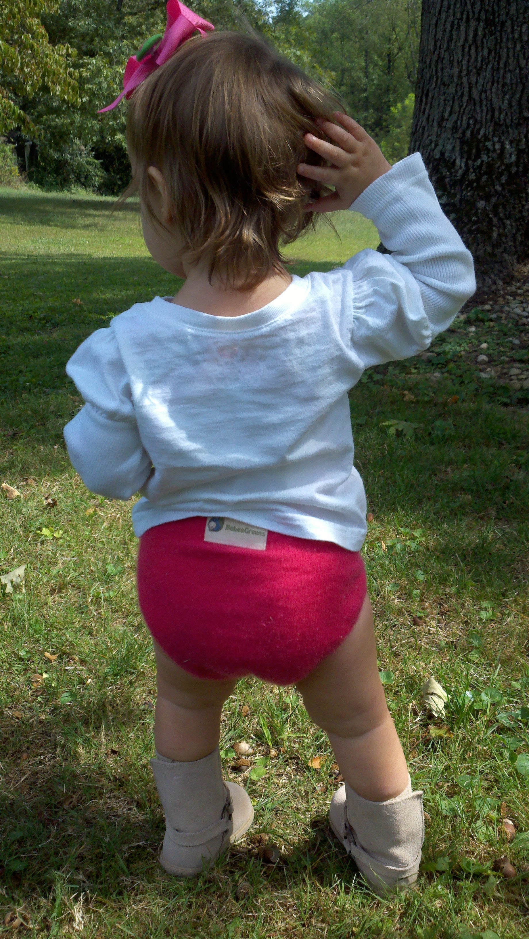 Child wearing a white long-sleeve shirt and pink diaper standing outdoors on grass.