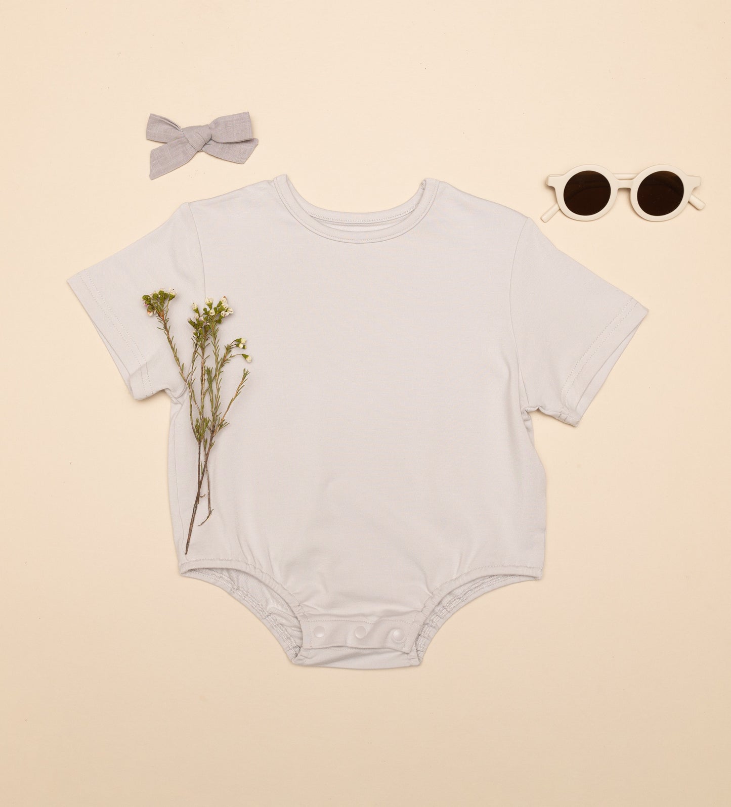 Baby onesie with a bow, sunglasses, and flowers on a beige background