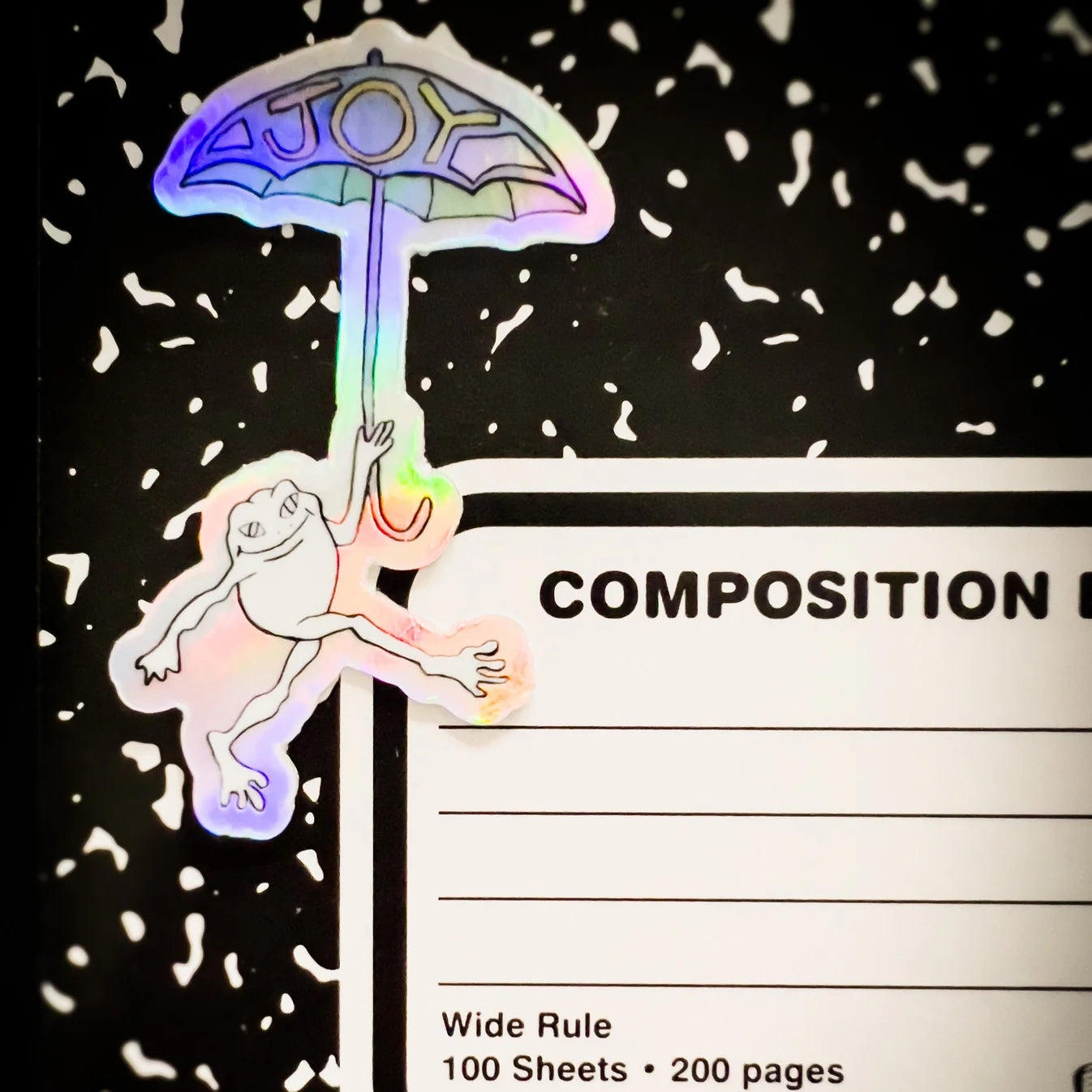 holographic joy frog sticker ona composition notebook