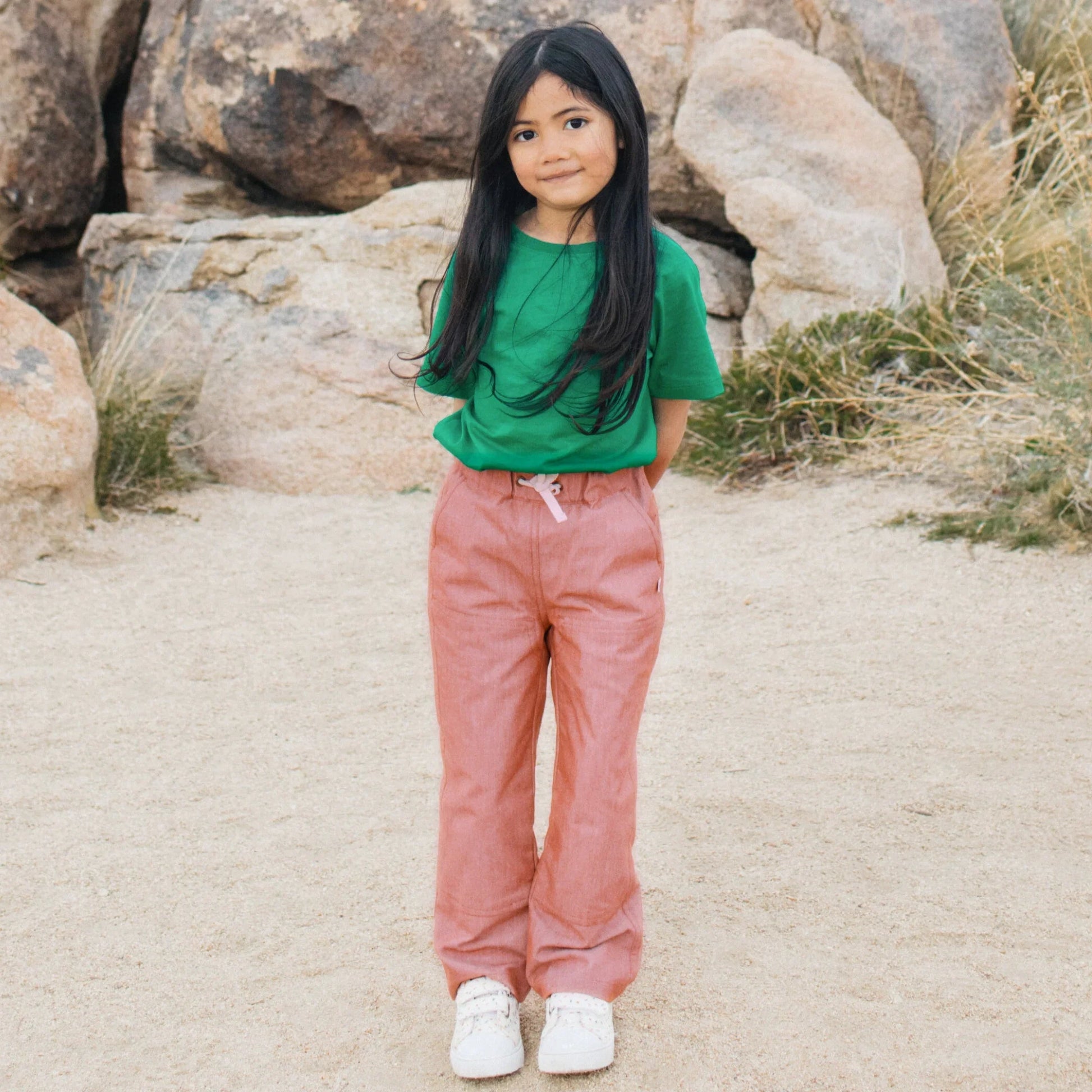 Child wearing a green shirt and pink pants standing in a rocky desert landscape