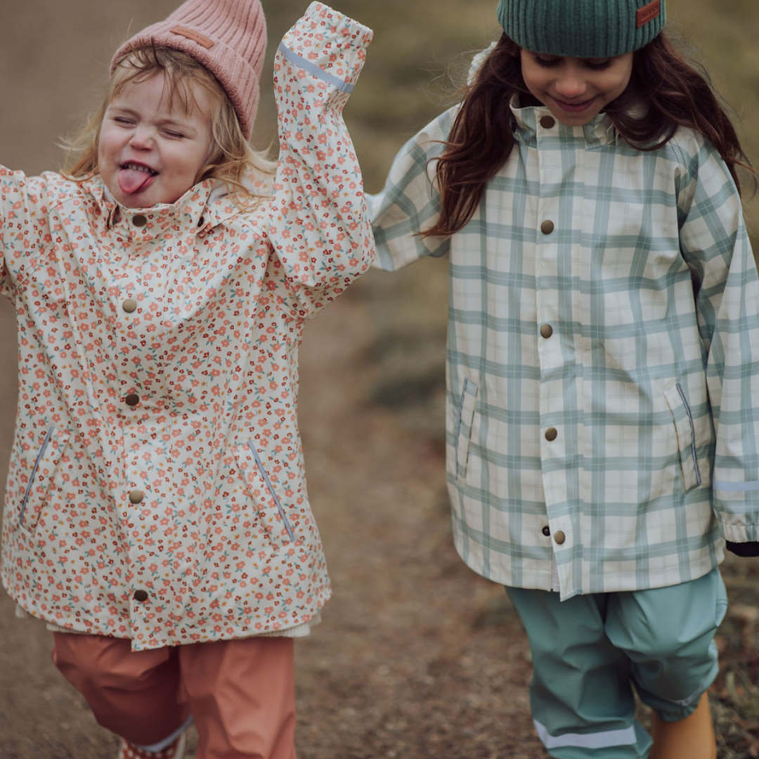 Two children in raincoats and hats standing outdoors on a blurred background