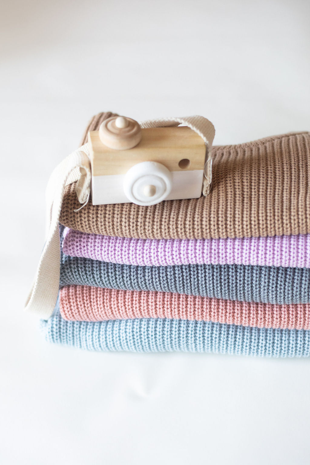 Stack of folded fabric with a wooden camera on top against a white background