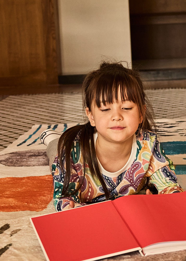 Child sitting on a rug with a red book open in front of them