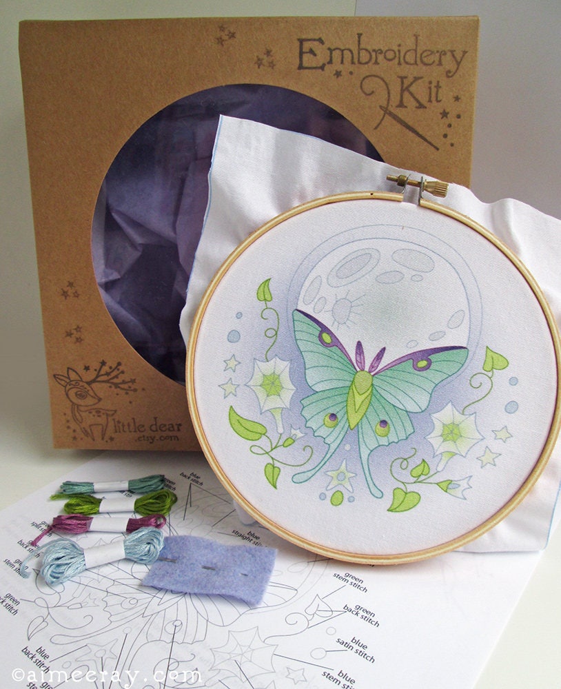Embroidery kit with a completed butterfly design in an hoop, surrounded by materials and instructions.