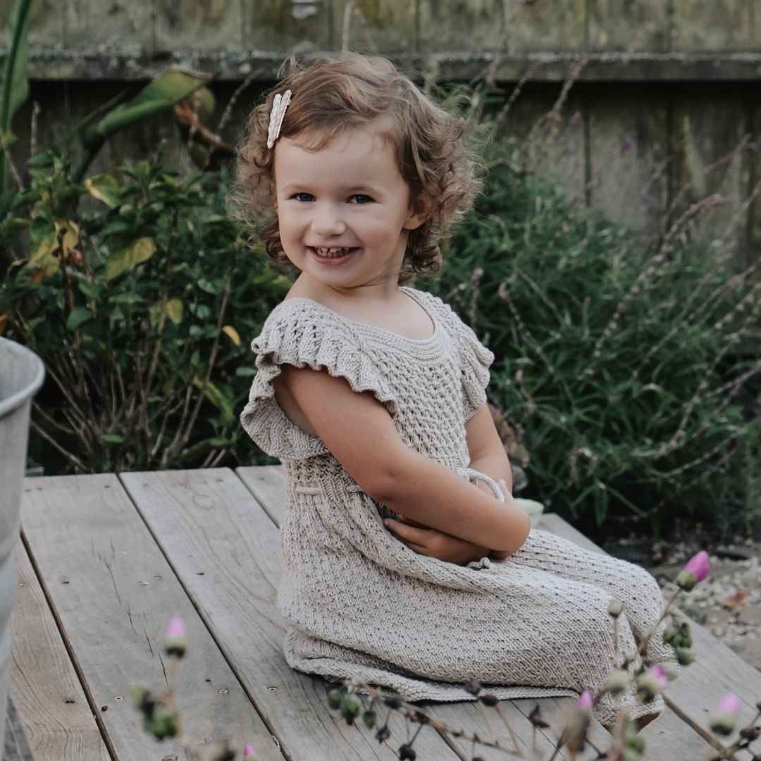 Young girl in a knitted dress sitting on a wooden bench outdoors.