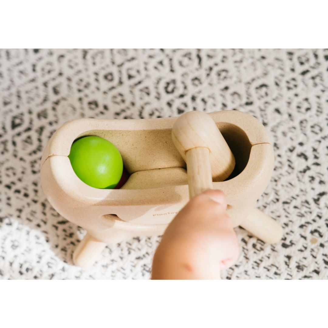 Wooden toy with a green ball and a handle on a speckled surface