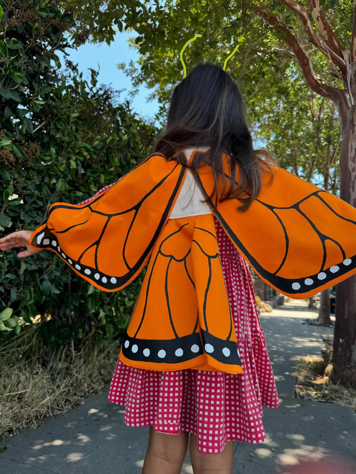 Person wearing a butterfly costume with orange wings and a pink dress outdoors.