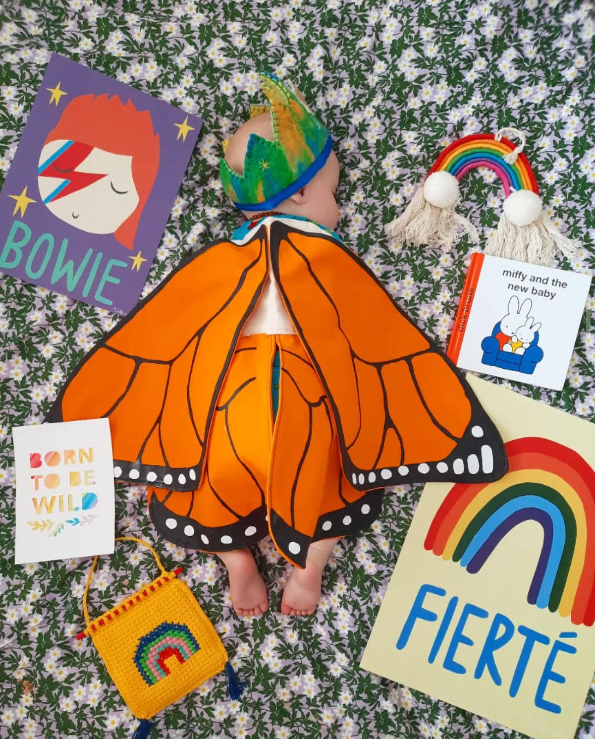 Child wearing a butterfly costume surrounded by children's books and toys on a textured surface