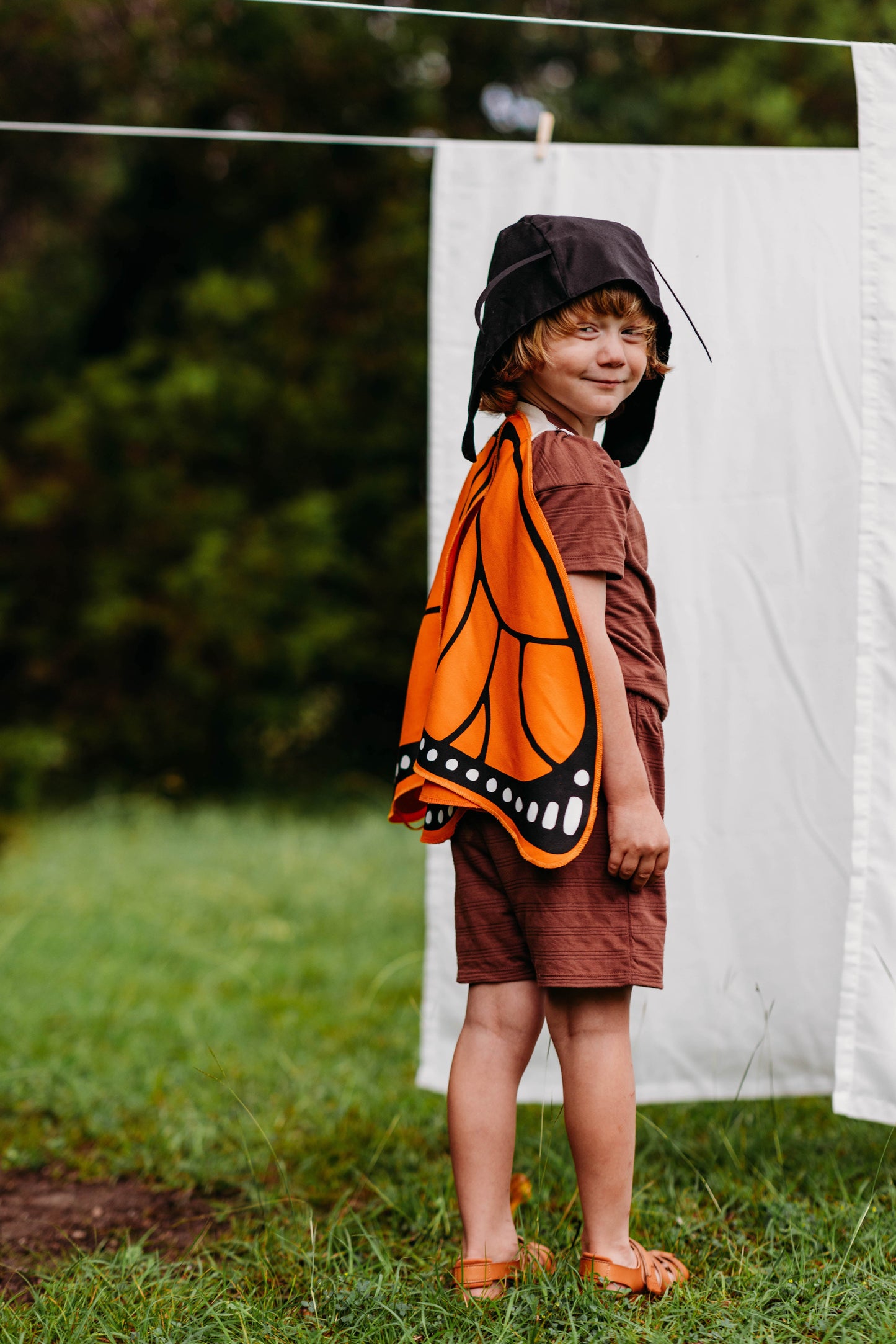 Child wearing a butterfly costume standing outdoors near a white sheet.