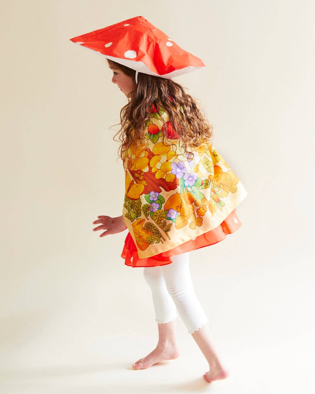 Child wearing a colorful dress with a mushroom hat on a plain background