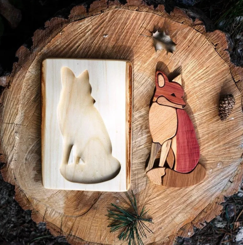 Wooden fox figurines on a wooden surface with pine needles and a pine cone.