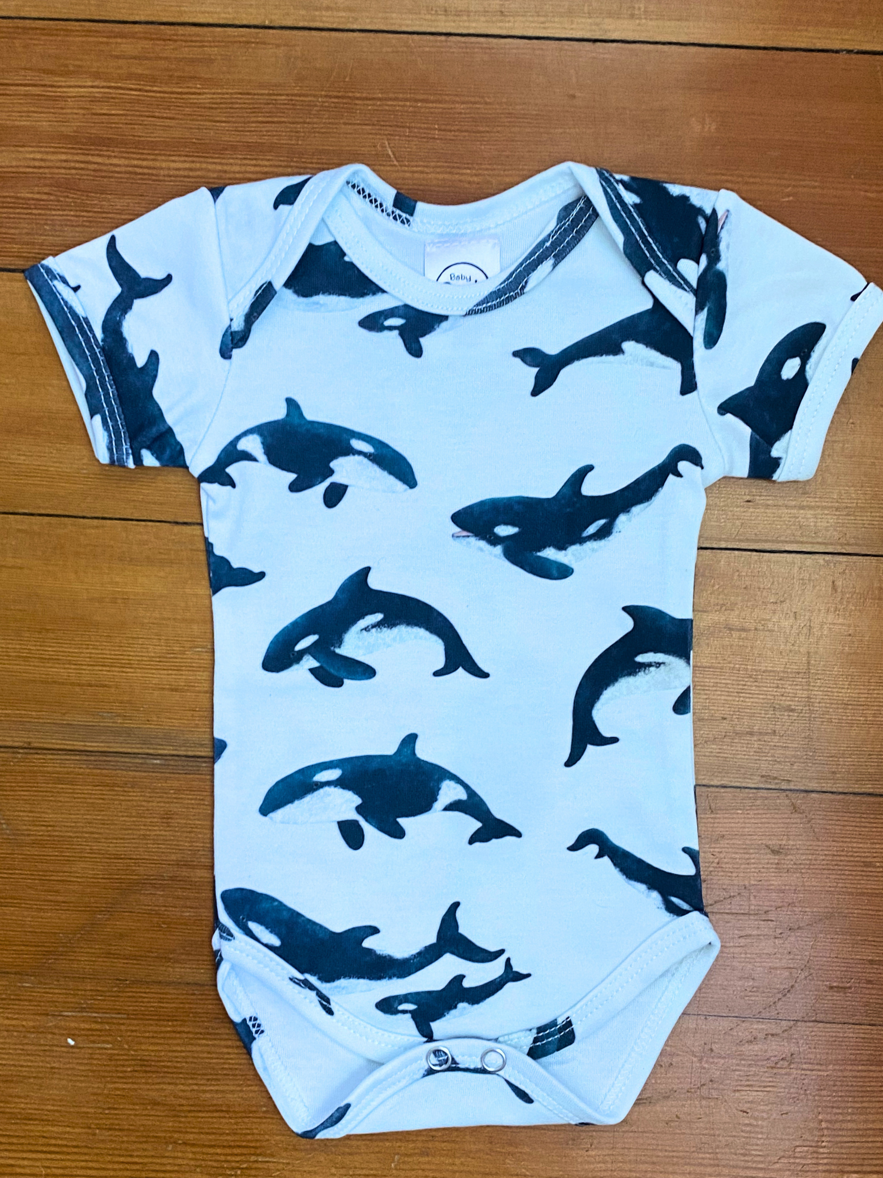 Baby onesie with blue whale pattern on a wooden surface