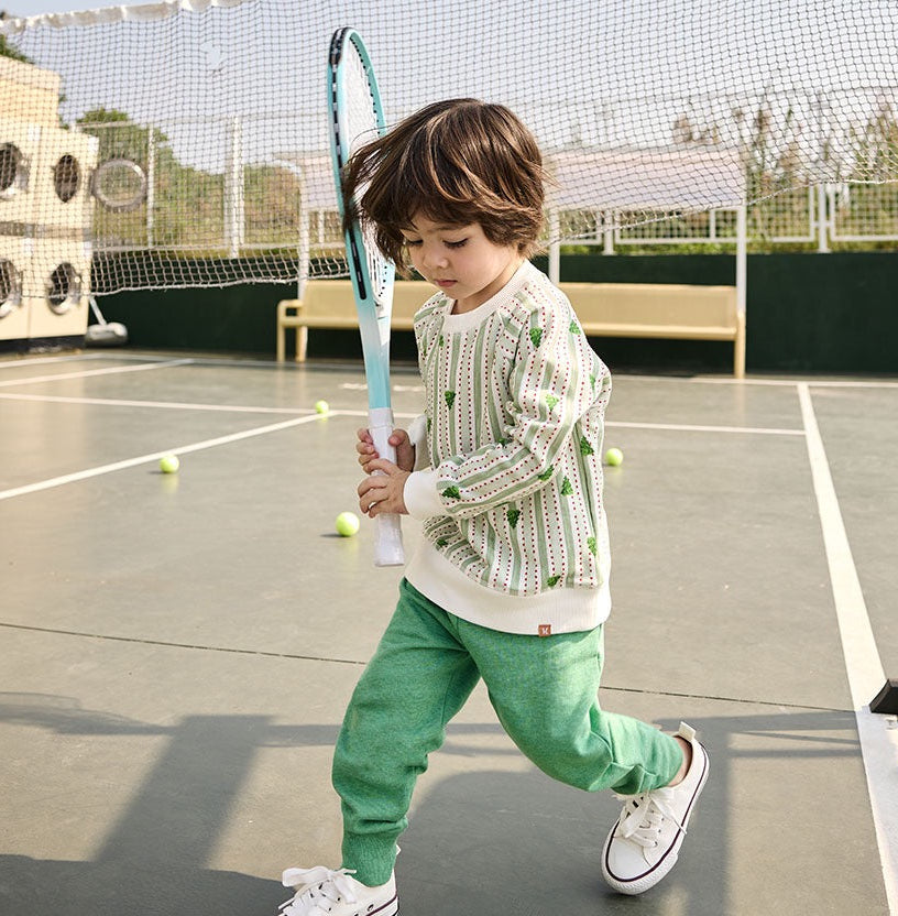 Child holding a tennis racket on a tennis court with tennis balls around