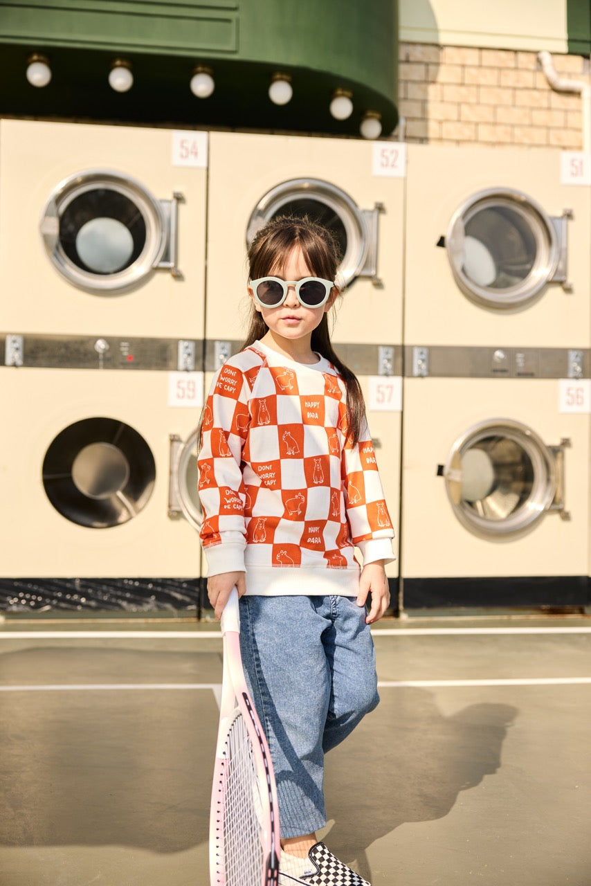 Child standing in front of a row of washing machines wearing a checkered shirt and sunglasses.