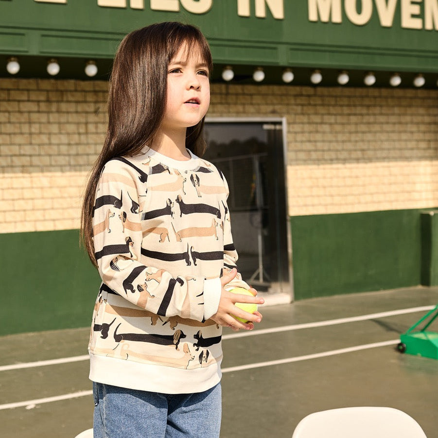 Child holding a tennis ball on a tennis court with a building in the background