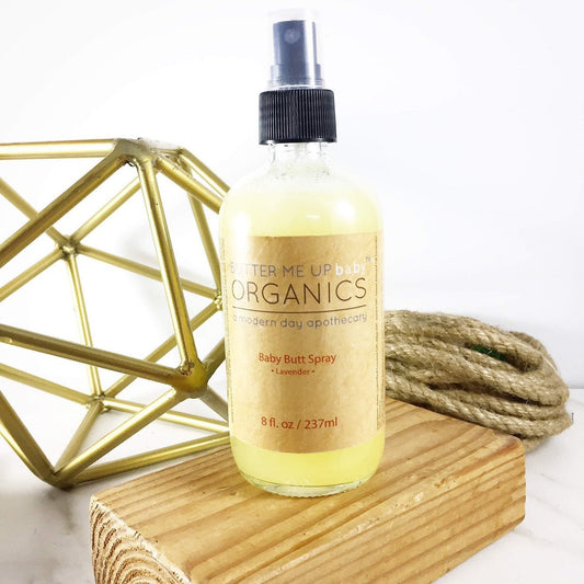 Bottle of Terme Up Organics Baby Butt Spray on a wooden block with geometric gold sculpture and rope in the background.