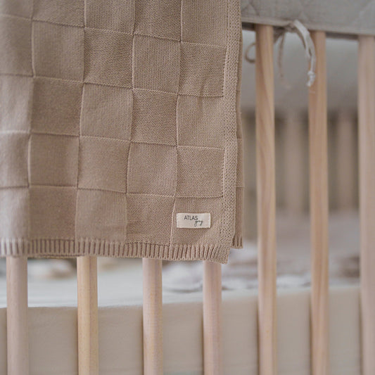 Textured brown blanket draped over a crib with a visible brand label.