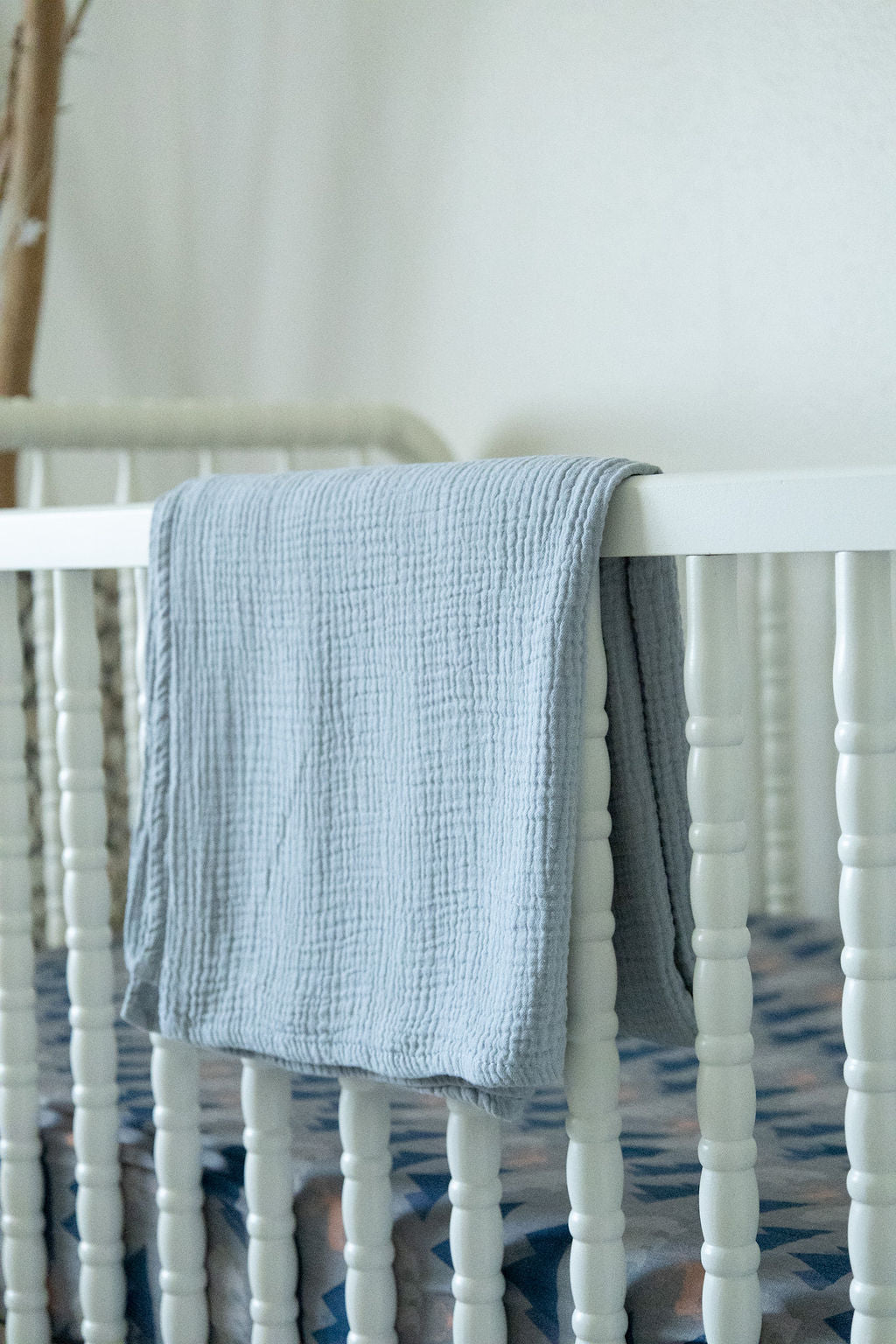 Blue textured blanket draped over a white crib with a blurred background