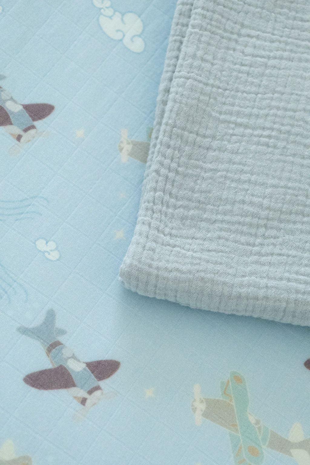 Light blue fabric with airplane patterns and a folded light gray blanket on top.