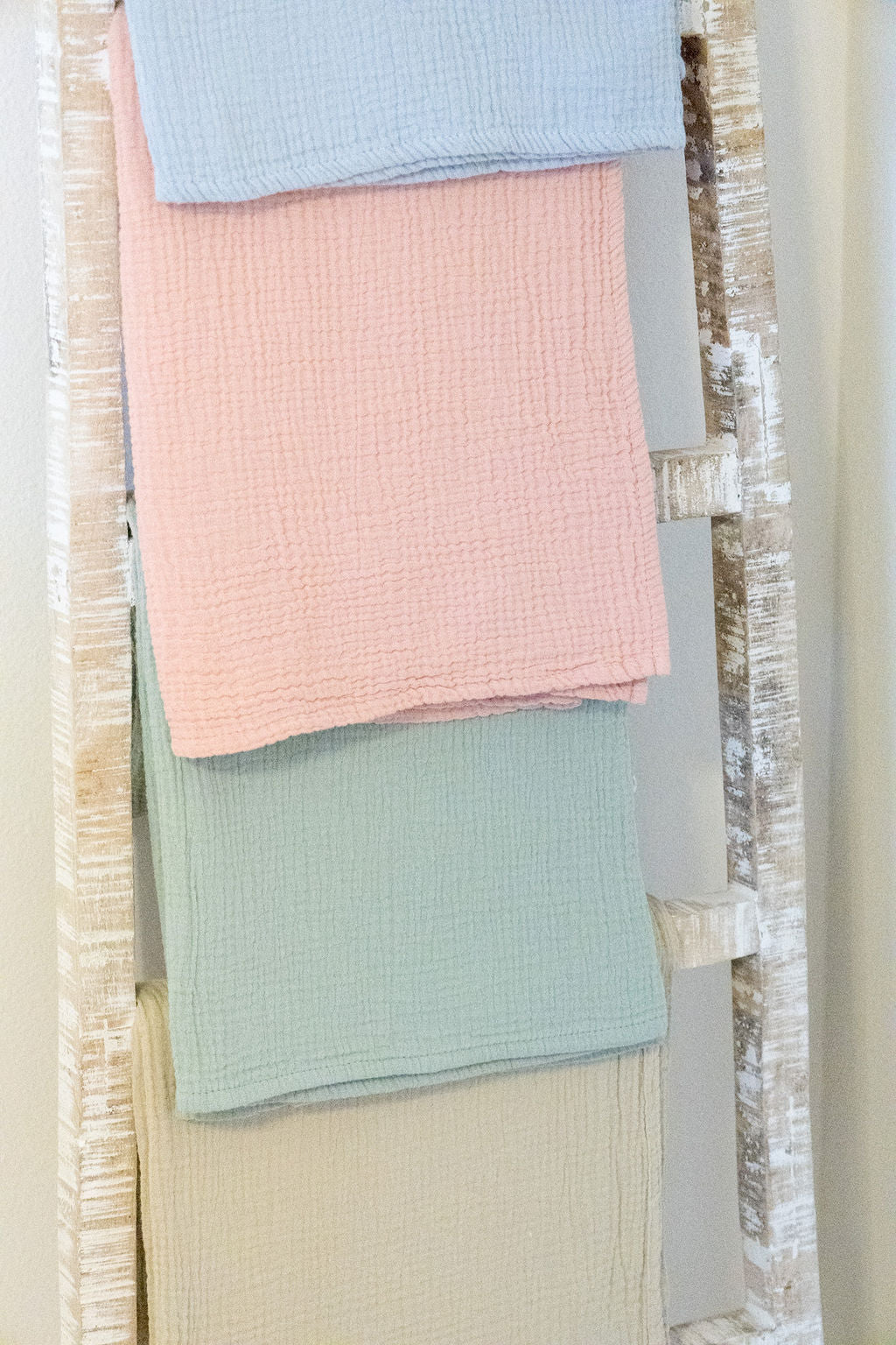 Stack of pastel-colored towels on a wooden ladder against a neutral wall.