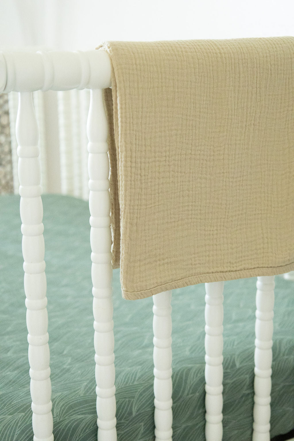 Beige blanket draped over a crib with a white and green textured mattress