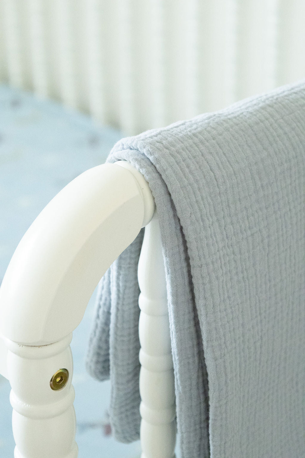 Gray textured blanket draped over a white chair arm with a blurred background