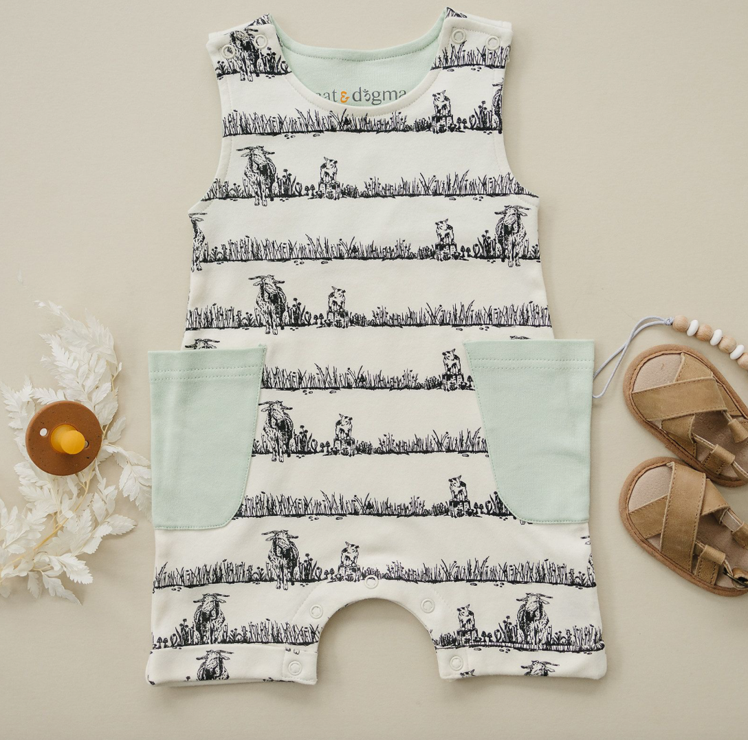 Baby romper with cow print and matching pouch on a beige surface