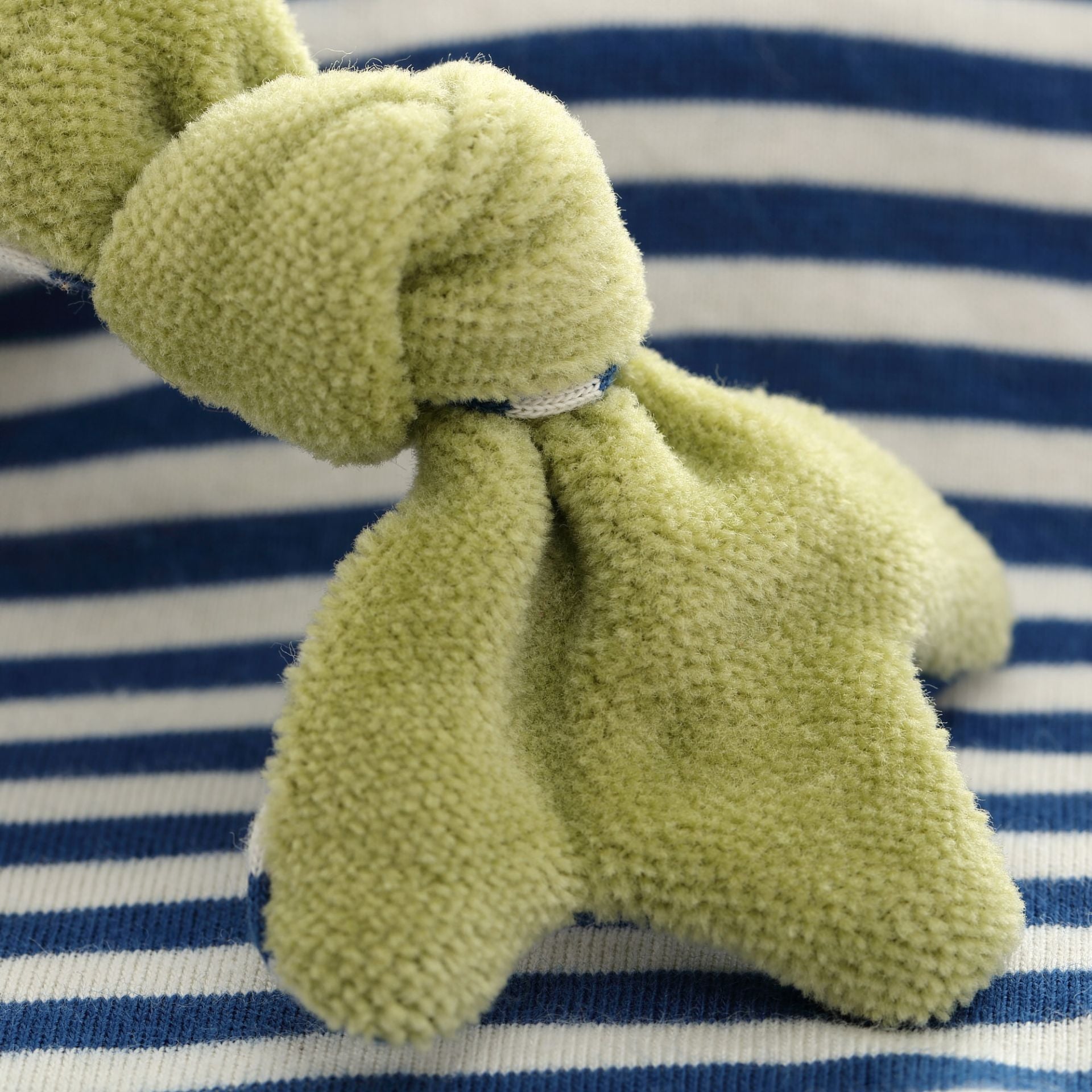 Green plush toy on a blue and white striped background