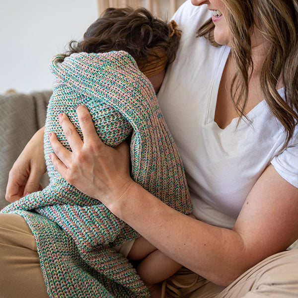 Woman holding a child wrapped in a colorful blanket on a couch.