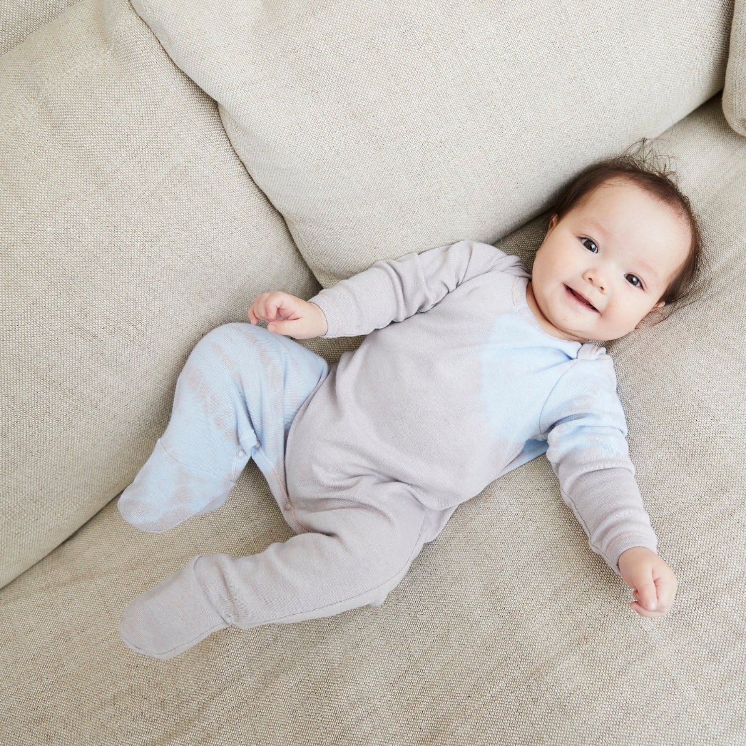 Baby in a light gray onesie lying on a beige couch