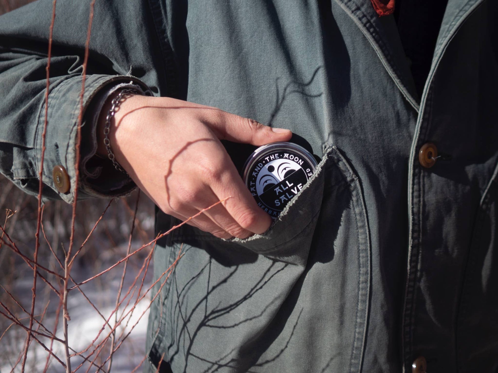 Person wearing a green jacket with a tin of All Salve in the pocket, standing outdoors.
