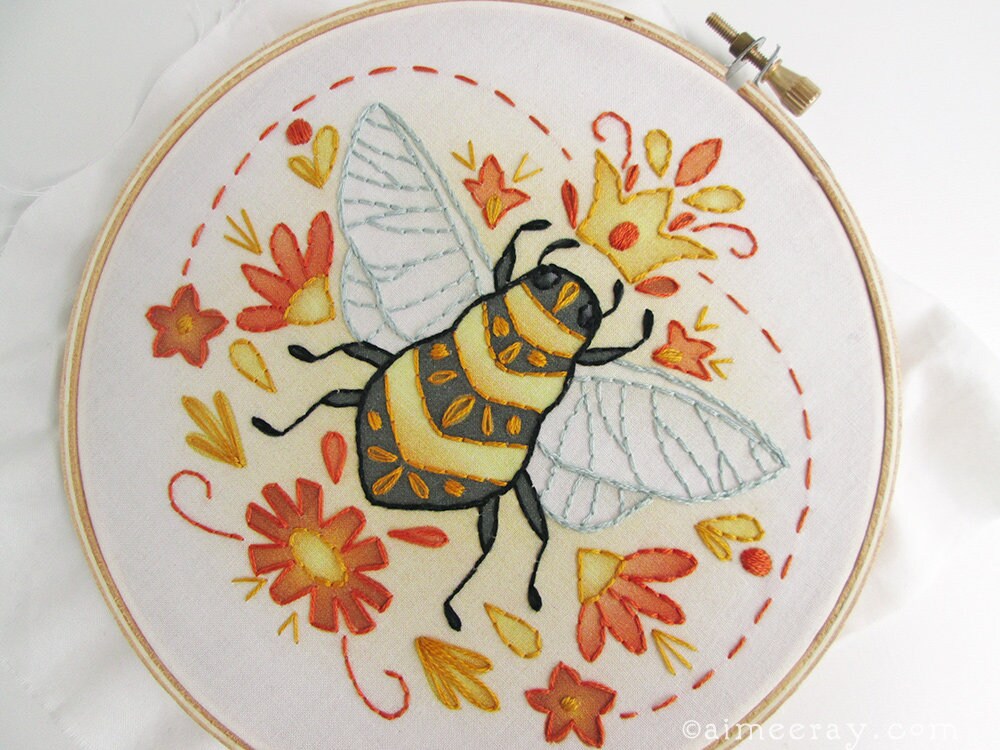 Embroidery hoop with a bee and floral design on white fabric