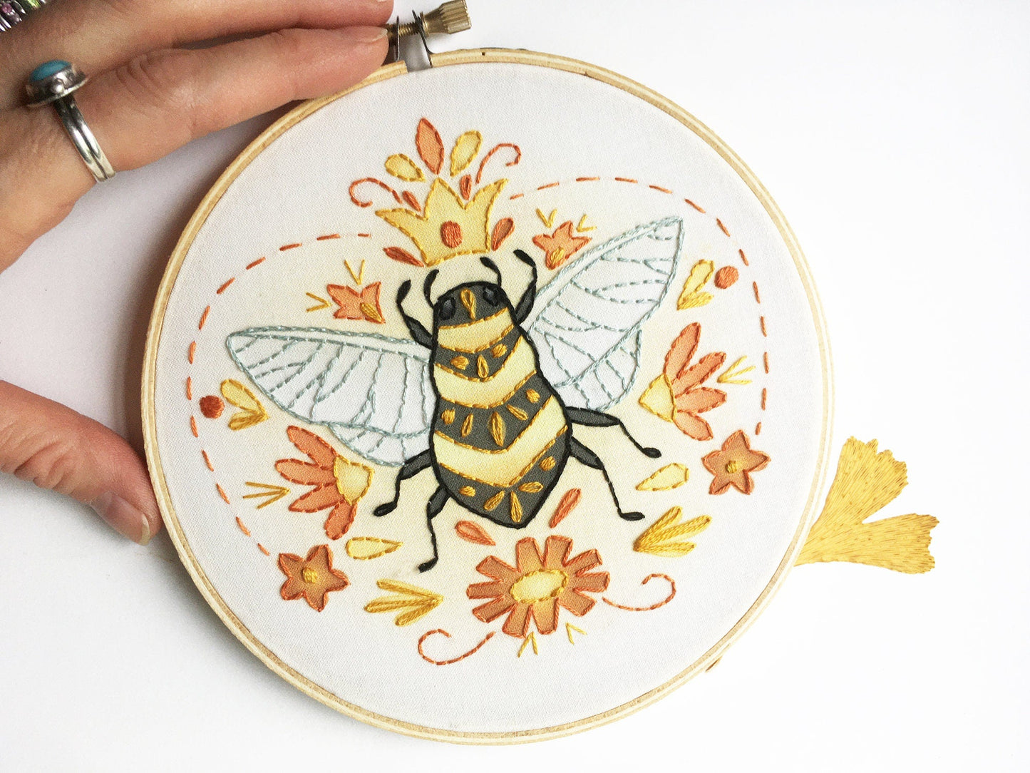 Embroidery hoop with a bee design held by a hand on a white background