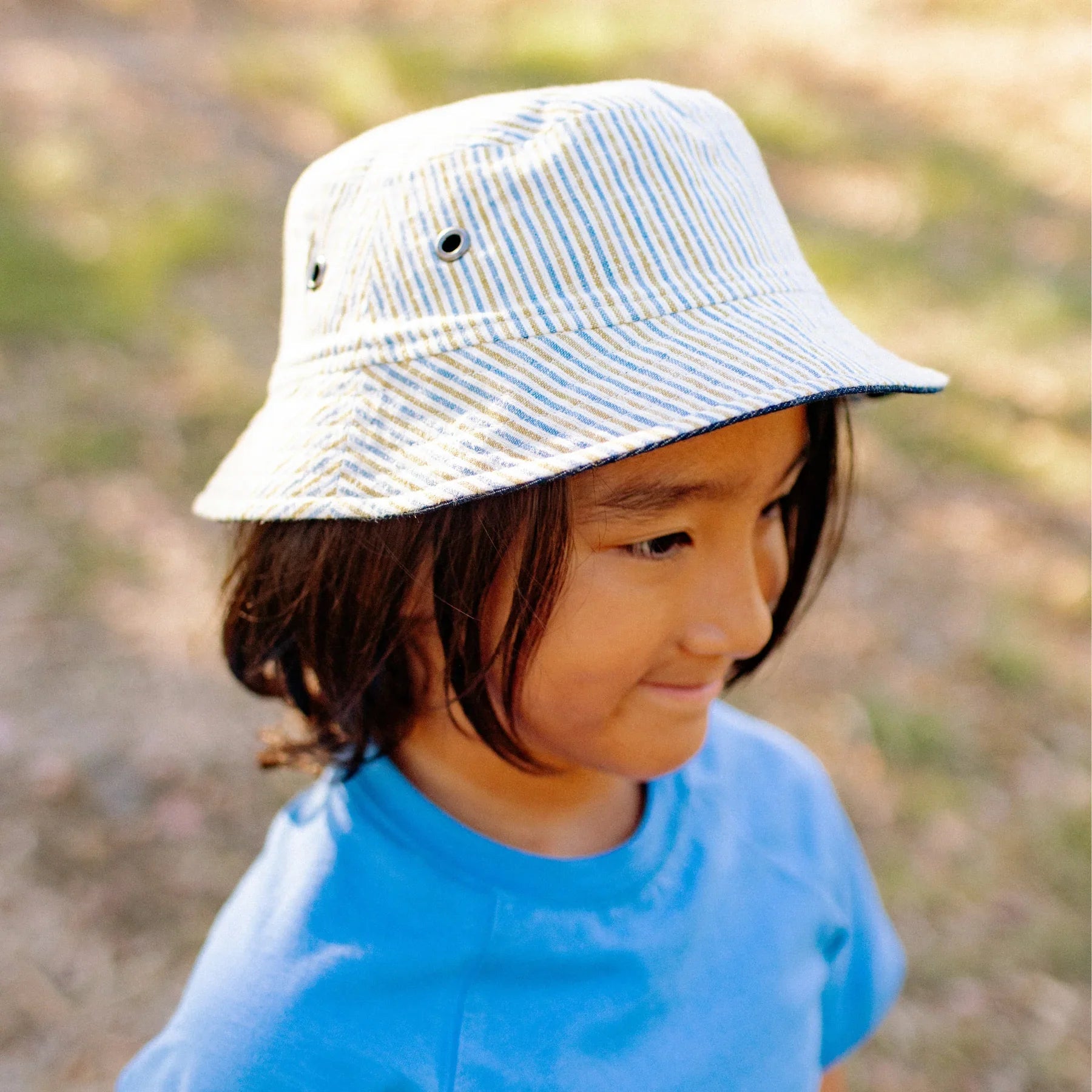 Child wearing a striped bucket hat and blue shirt outdoors