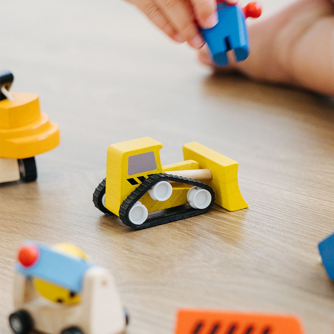Children's toy bulldozer on a wooden surface with a hand reaching in.