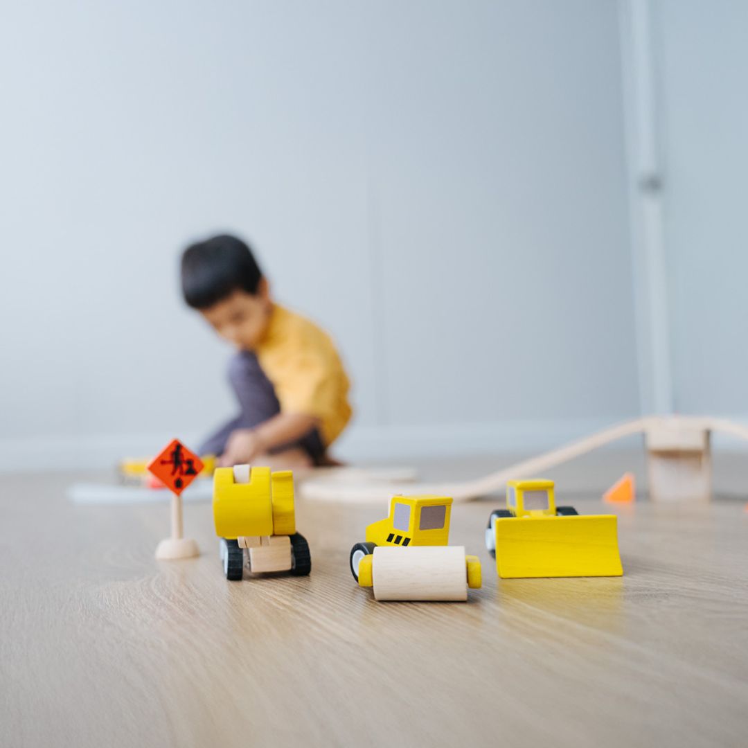 Children's toy construction vehicles on a table with a blurred child in the background.