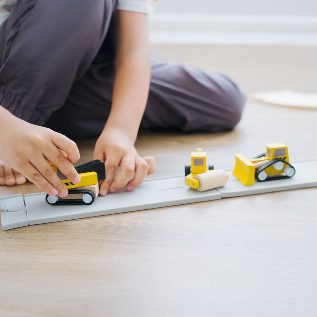 Child playing with toy construction vehicles on a wooden floor