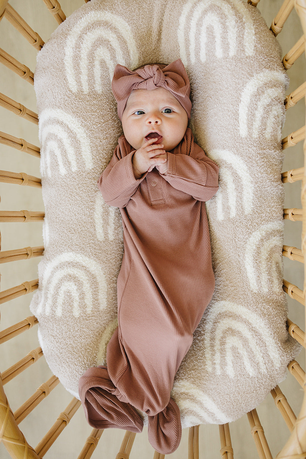 Baby in a pink outfit lying on a textured blanket in a wooden crib