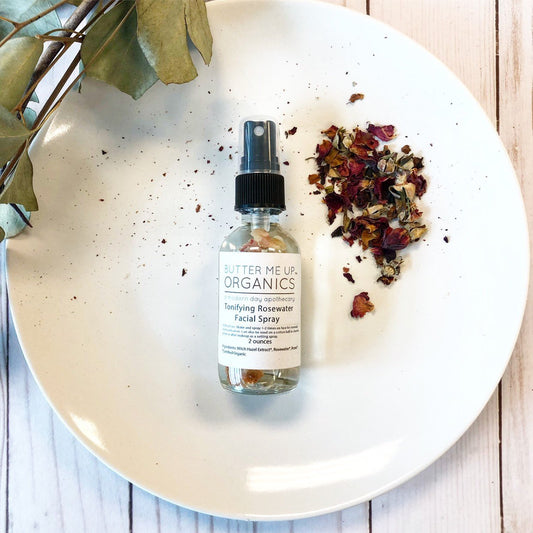 Bottle of Butter Me Up Organics facial spray on a white plate with dried flowers and leaves.