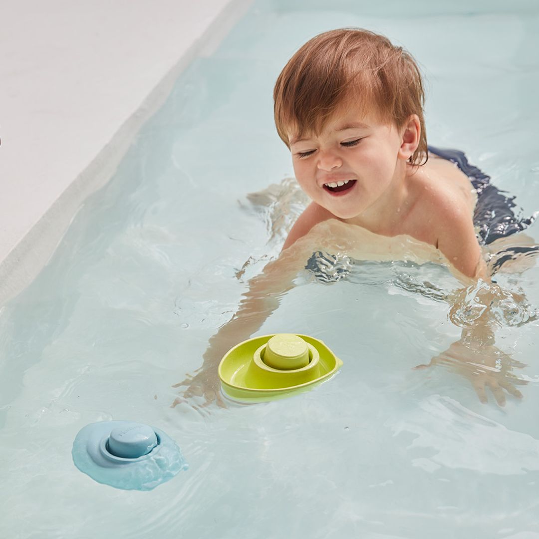 Child playing with a green toy in a bathtub