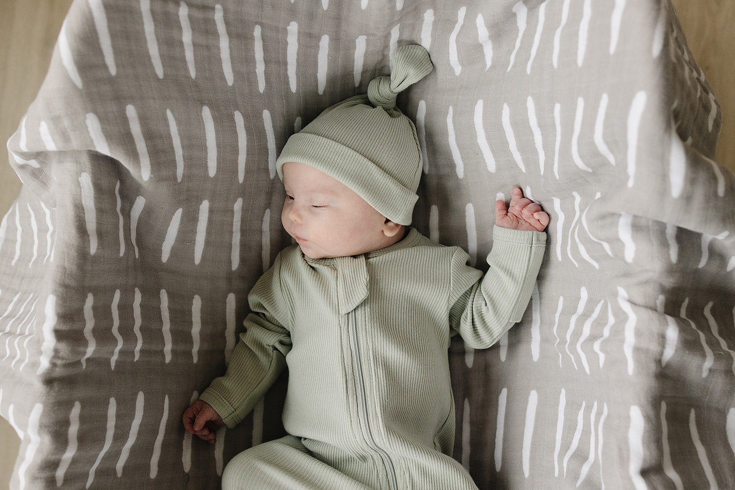Baby in a green outfit and hat lying on a patterned blanket