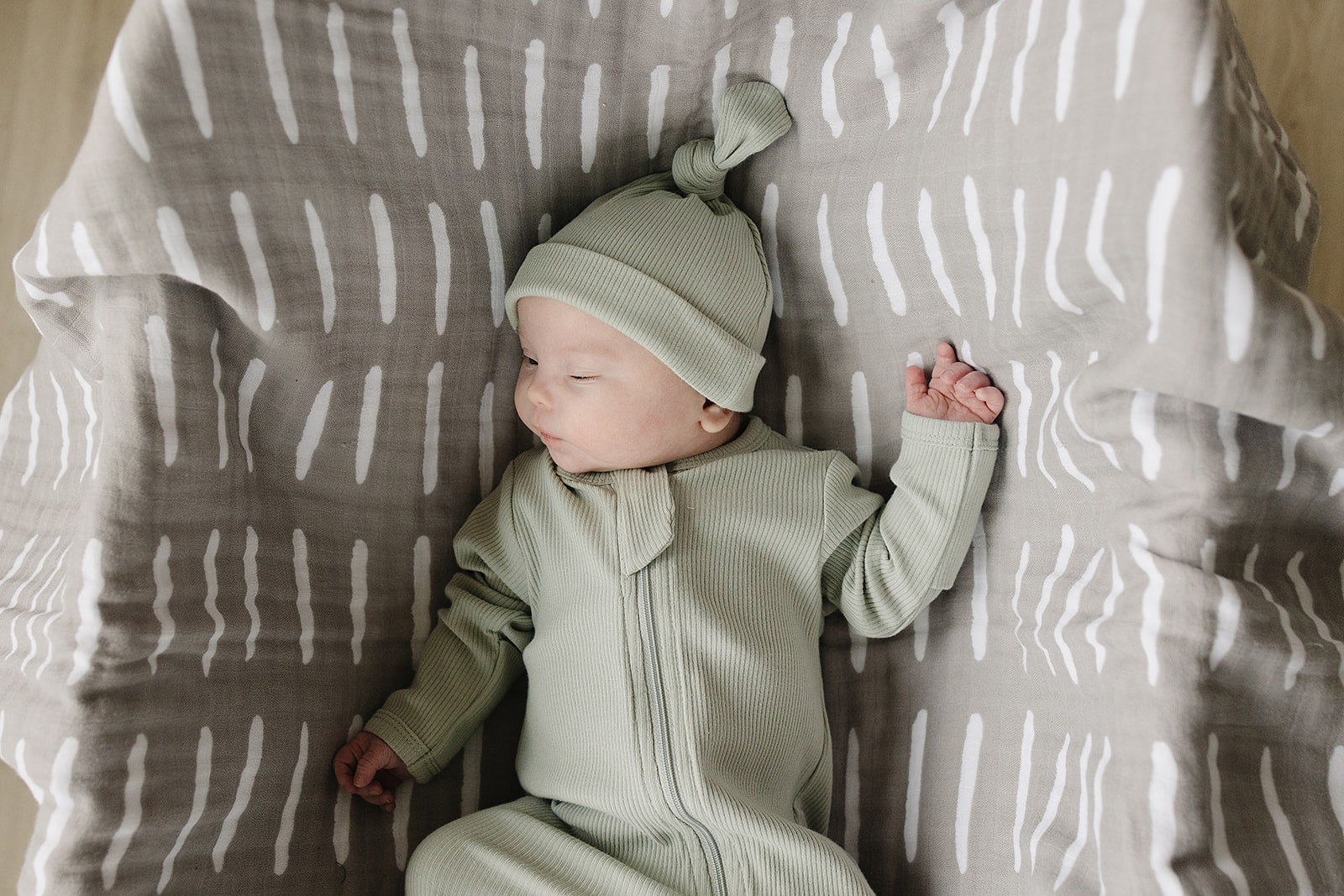 Baby in a green outfit and hat lying on a patterned blanket